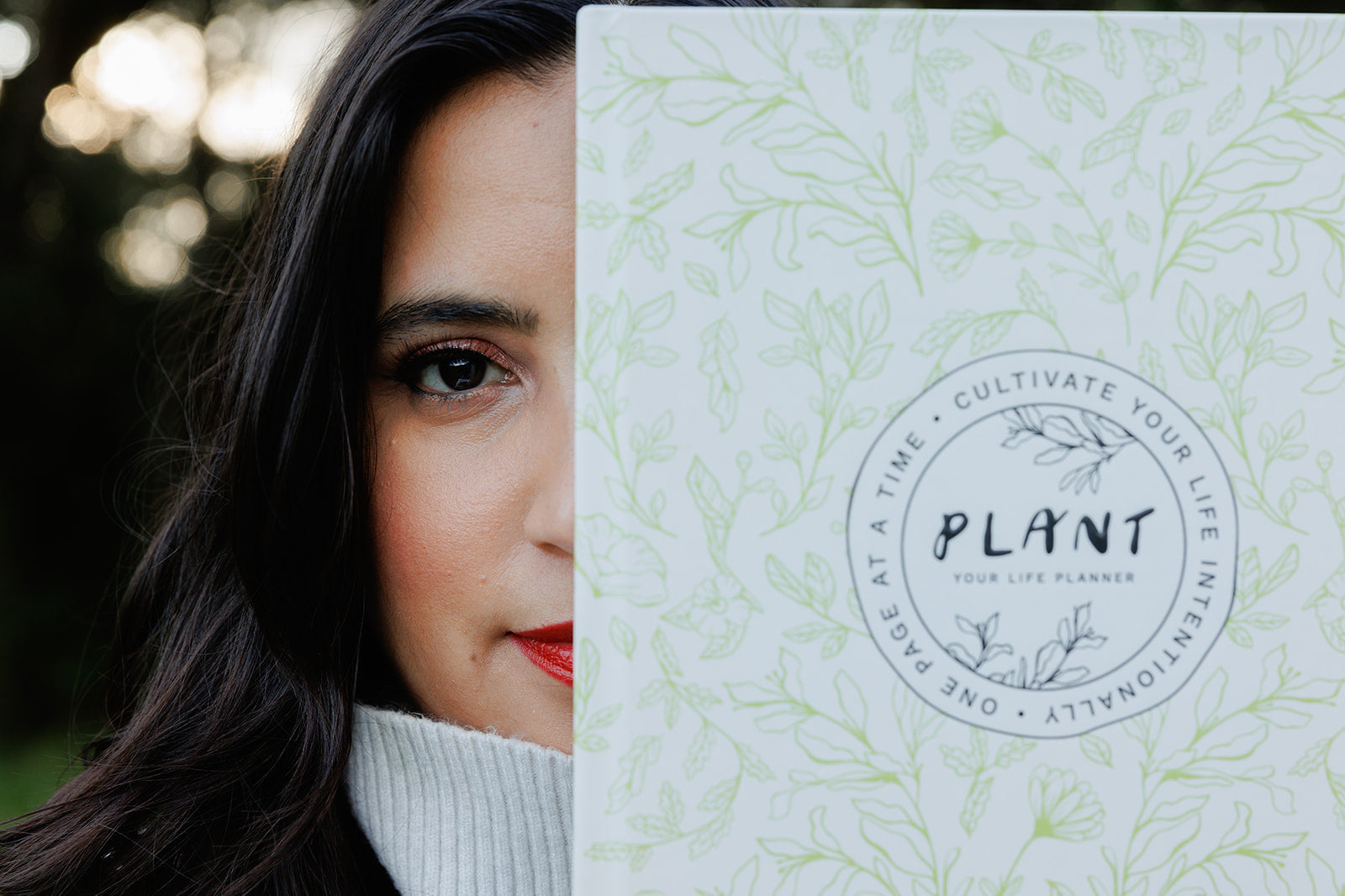 A close-up of a woman’s face partially hidden behind the "PLANT: Your Life Planner," with only one eye visible. The planner’s botanical design is in focus, symbolizing clarity, vision, and intentional living.