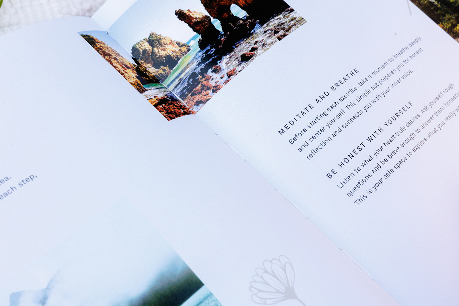 A close-up of an open planner featuring a mindfulness exercise with the text "Meditate and Breathe" and "Be Honest With Yourself." The page includes scenic photography of a rocky shoreline, symbolizing reflection, self-awareness, and inner peace.